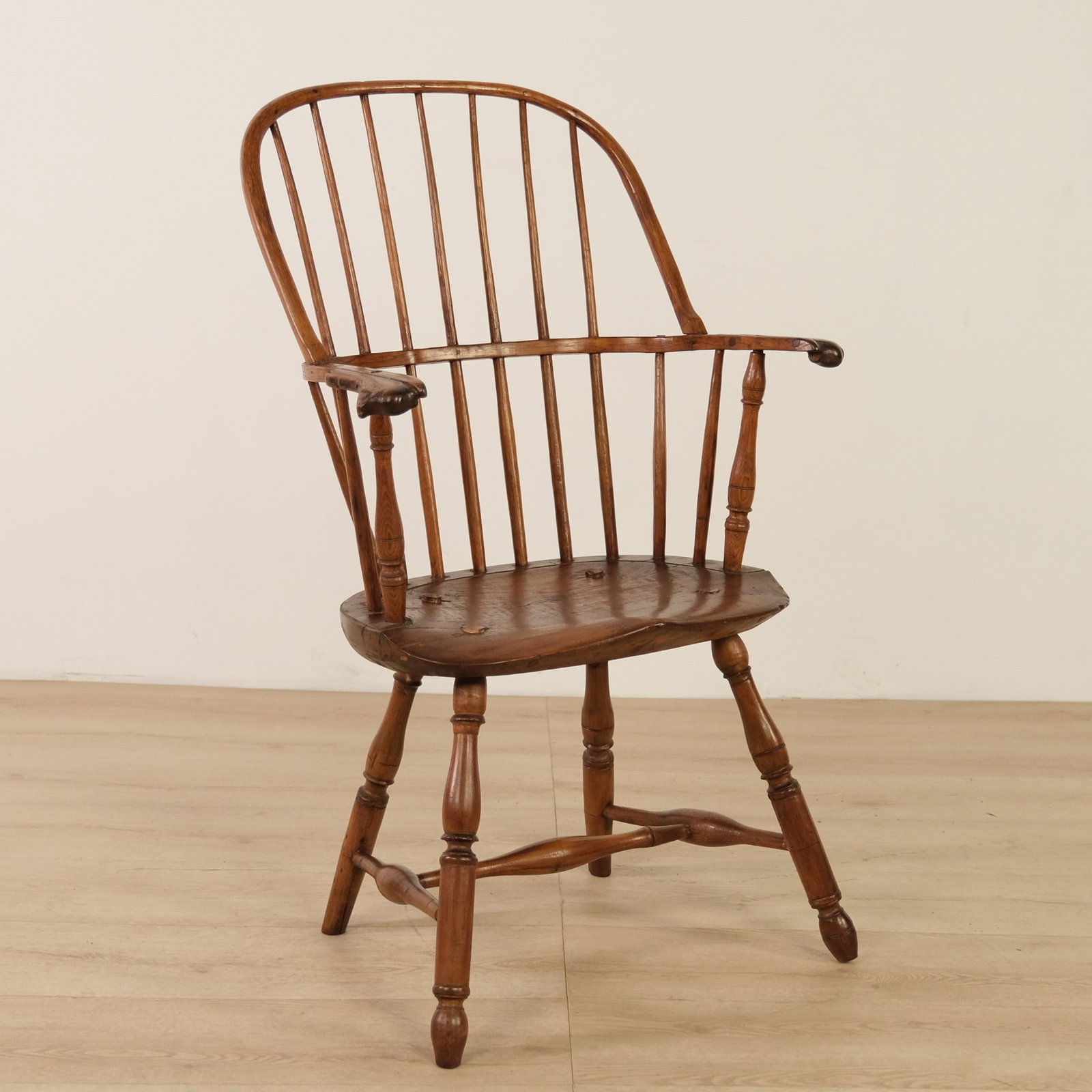 Knuckle Arm Wood Windsor Chair: A warm-toned Windsor chair featuring a steam-bent wooden arm rail ending in finely carved, scroll-like "knuckle" handholds. Sculpted saddle seat with turned splayed legs.