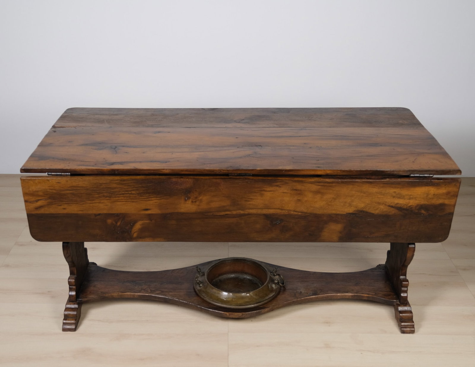 Victorian Drop Leaf Table, c. 1880: An 1880's Victorian utility drop-leaf table featuring a brass or bronze wash-basin ring with securing tabs, a distinctive original feature. The table rests on bold, bracketed trestle ends with