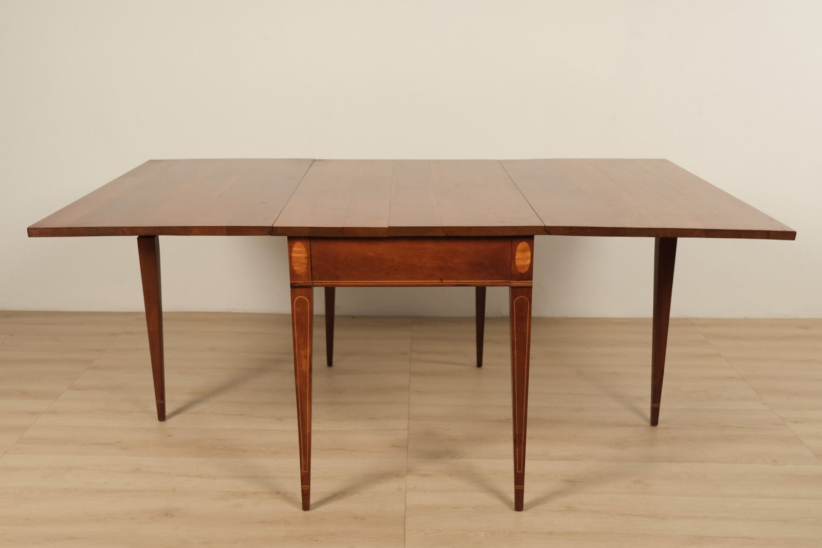 Hepplewhite style cherry drop leaf dining table, c. 18th century: A Hepplewhite-style cherry drop-leaf dining table capturing the refined character of the late 18th-century Federal period. Its slender tapered legs, warmly toned cherry surface, and hinged leaves