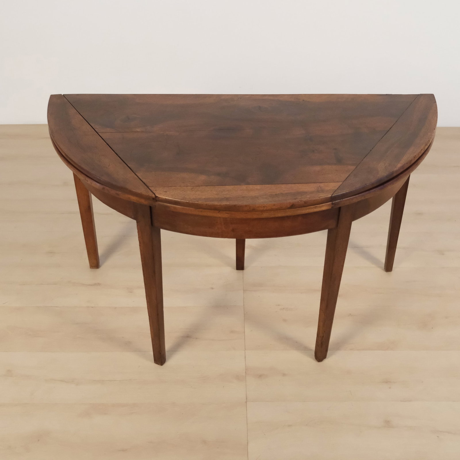 Half Moon Wood Console Table: A vintage demilune console table featuring a half-moon top with a shaped perimeter, simple tapered legs and a clean silhouette. The top is constructed with fold-over leaves allowing it to open into a