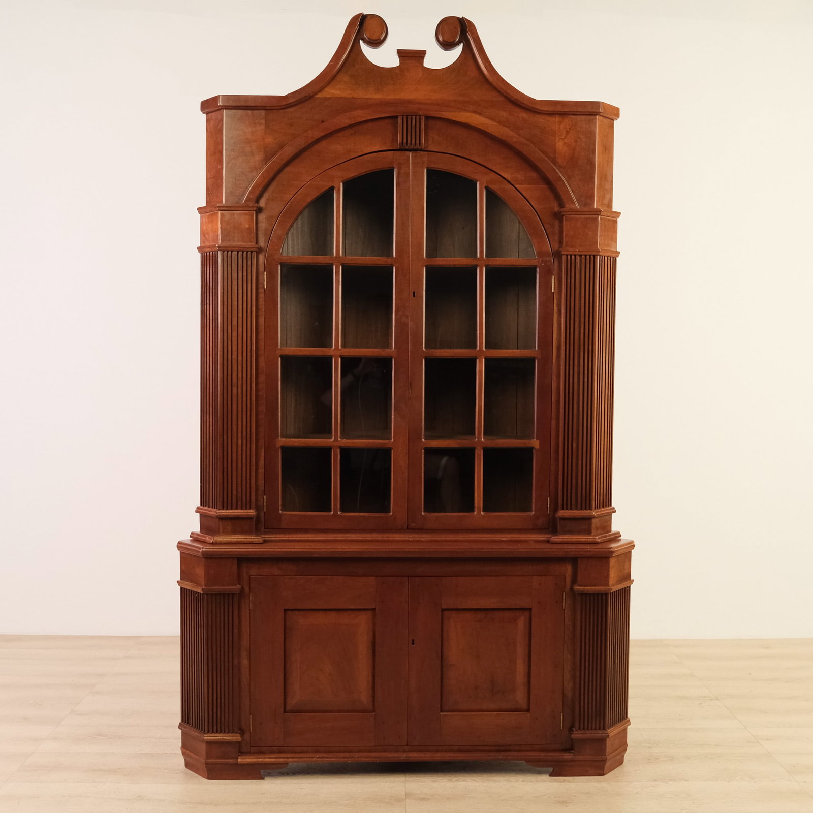 Antique Federal Cherry Corner Cabinet: This is a tall, formal, Federal-style, solid cherry corner cabinet with a strong architectural presence. The upper section features a broken-scroll pediment and arched glazed doors. Lower doors are