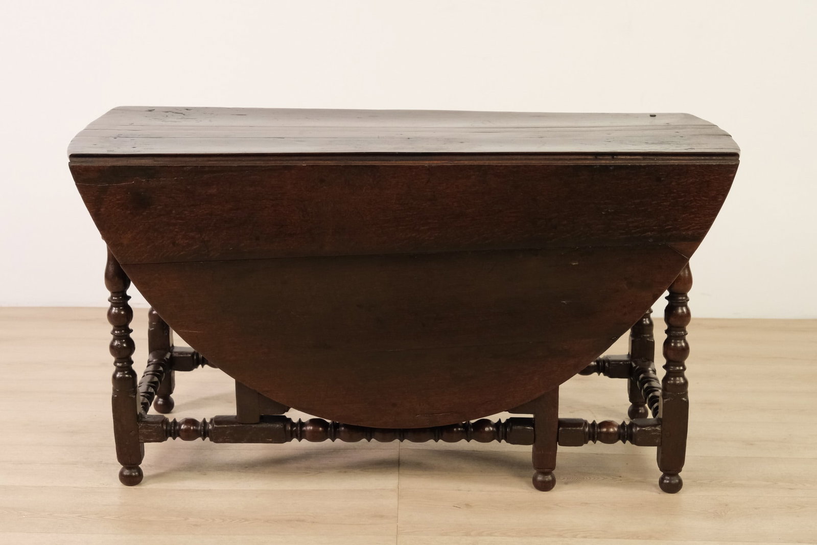 William and Mary Drop-Leaf Wood Table: A charming William & Mary-style drop-leaf table in a warm dark wood finish, with a compact rectangular form that opens into an oval dining table. When closed it has a narrow footprint. The classic