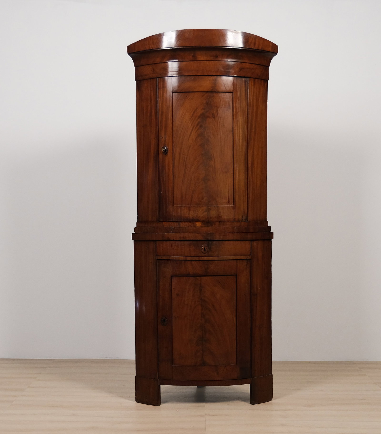 Italian Bow-Front Corner Cabinet in Flame Figured Mahogany: Elegant Italian corner cabinet with a bow-front form, featuring a domed top above two paneled doors showcasing dramatic flame-figured mahogany veneer. A single drawer with a brass keyhole escutcheon