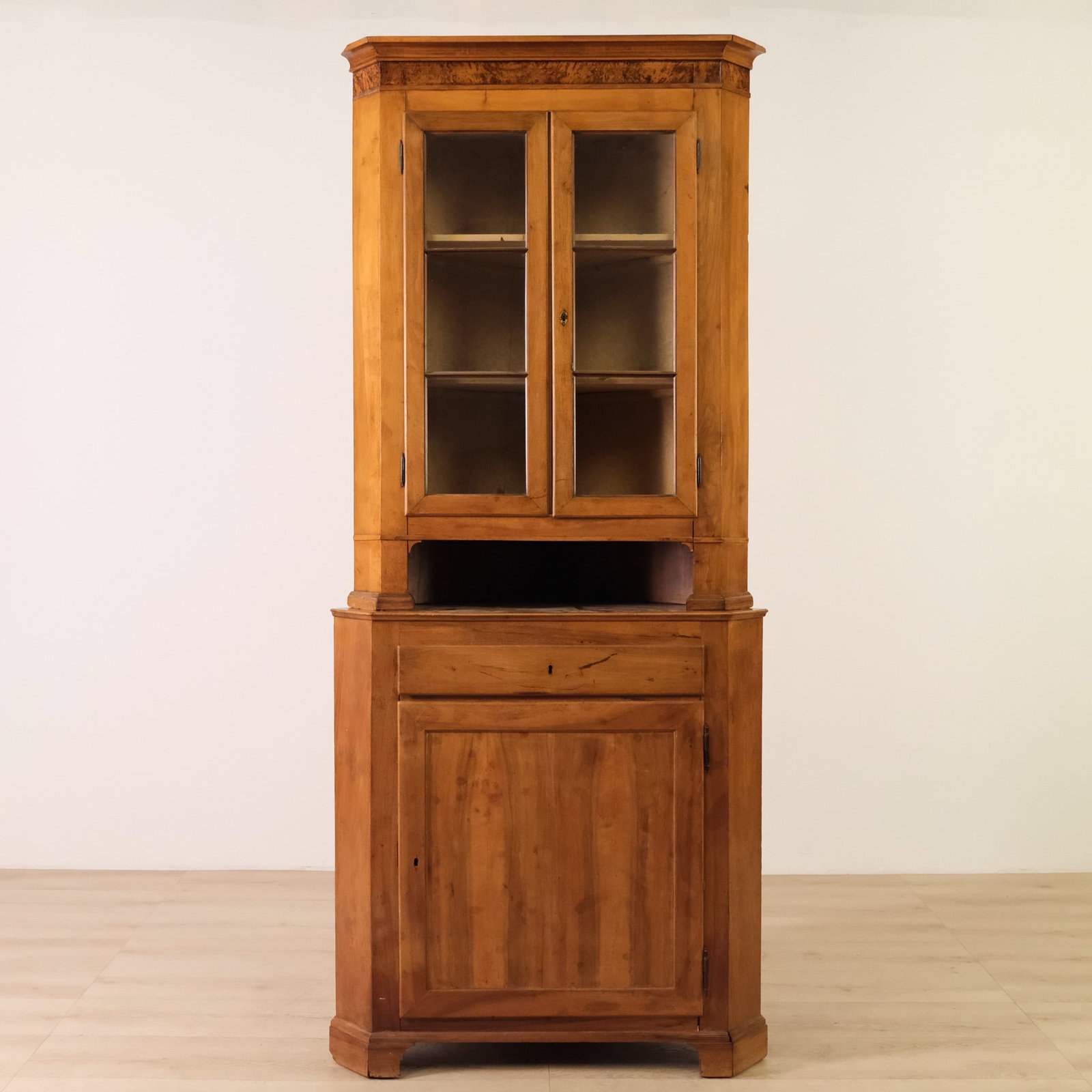 Antique Two Piece Continental Chestnut Corner Cupboard, c. Mid-19th Century: This is a mid-19th century corner cupboard, with a glazed upper cabinet over a lower enclosed base.?Shaped to fit into a corner with a flat front and angled sides, rising on a simple molded plinth