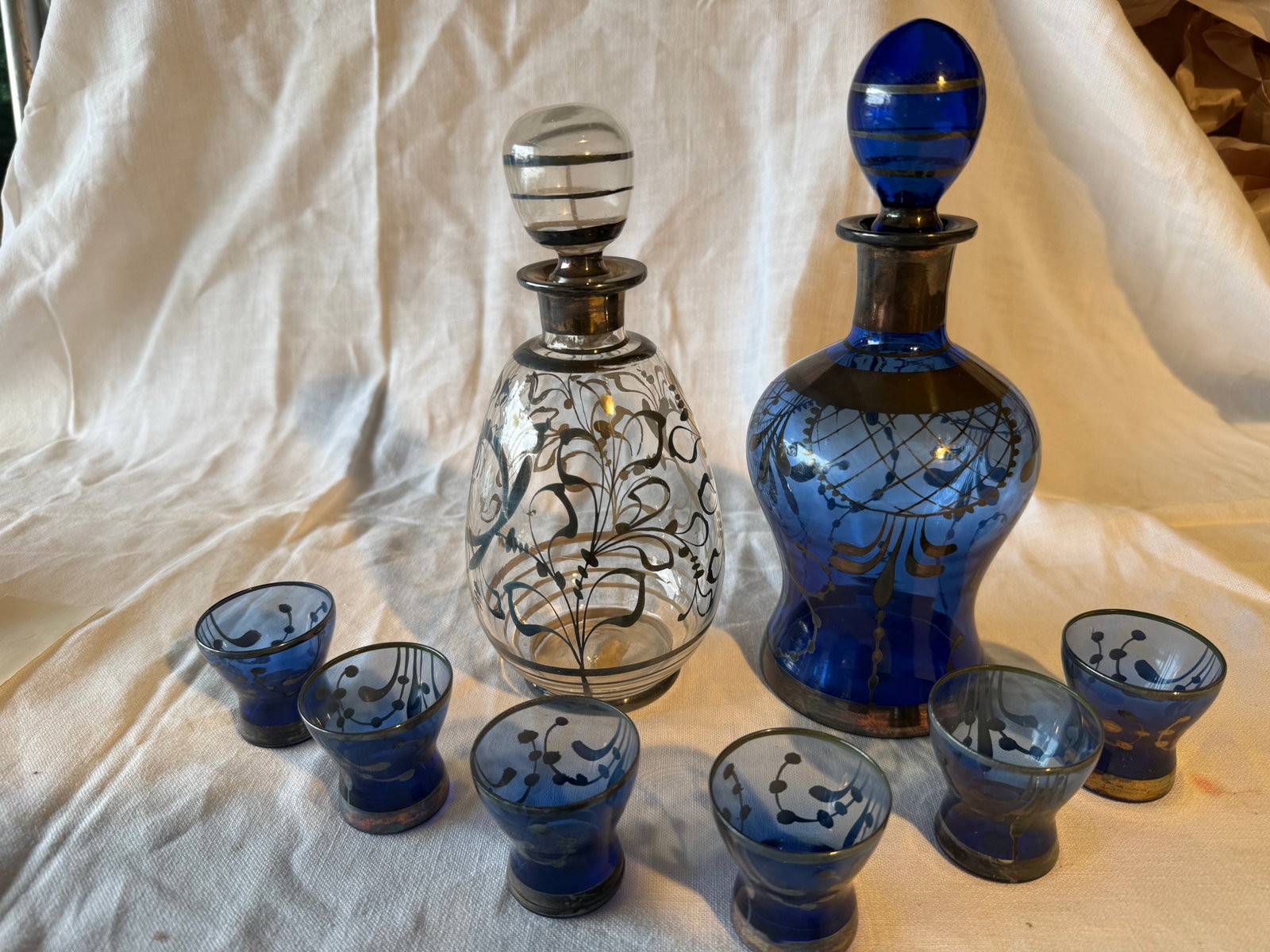 Antique Glass Decanters and Glasses: Florence, Italy. Dimensions: Blue Decanter- 6.5in H x 3.25in W. Clear Decanter- 6.5in H x 3.25in W. Glasses- 2in H x 2in W. Some wear as pictured.