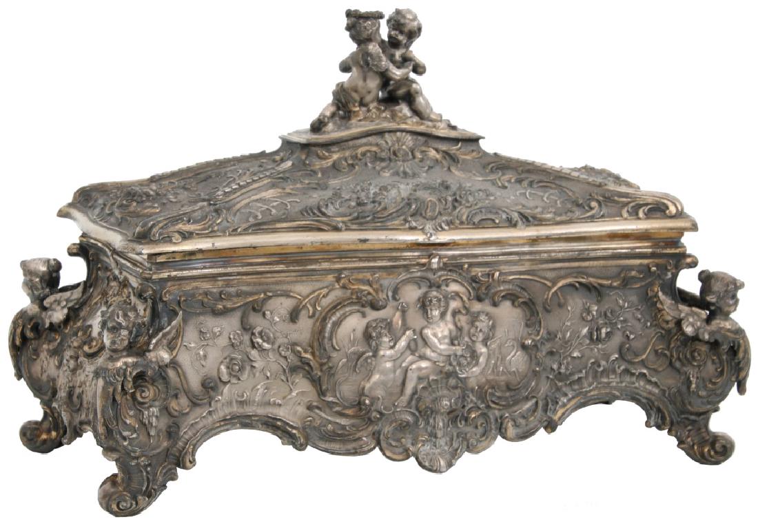 WMF Silver Plated Jewelry Casket: WMF Silver Plated Jewelry Casket. The large silver plated chest has a hinged lid with 2 nude figural winged putti seated on top; relief decorated flowers and filigree with relief front panels depictin