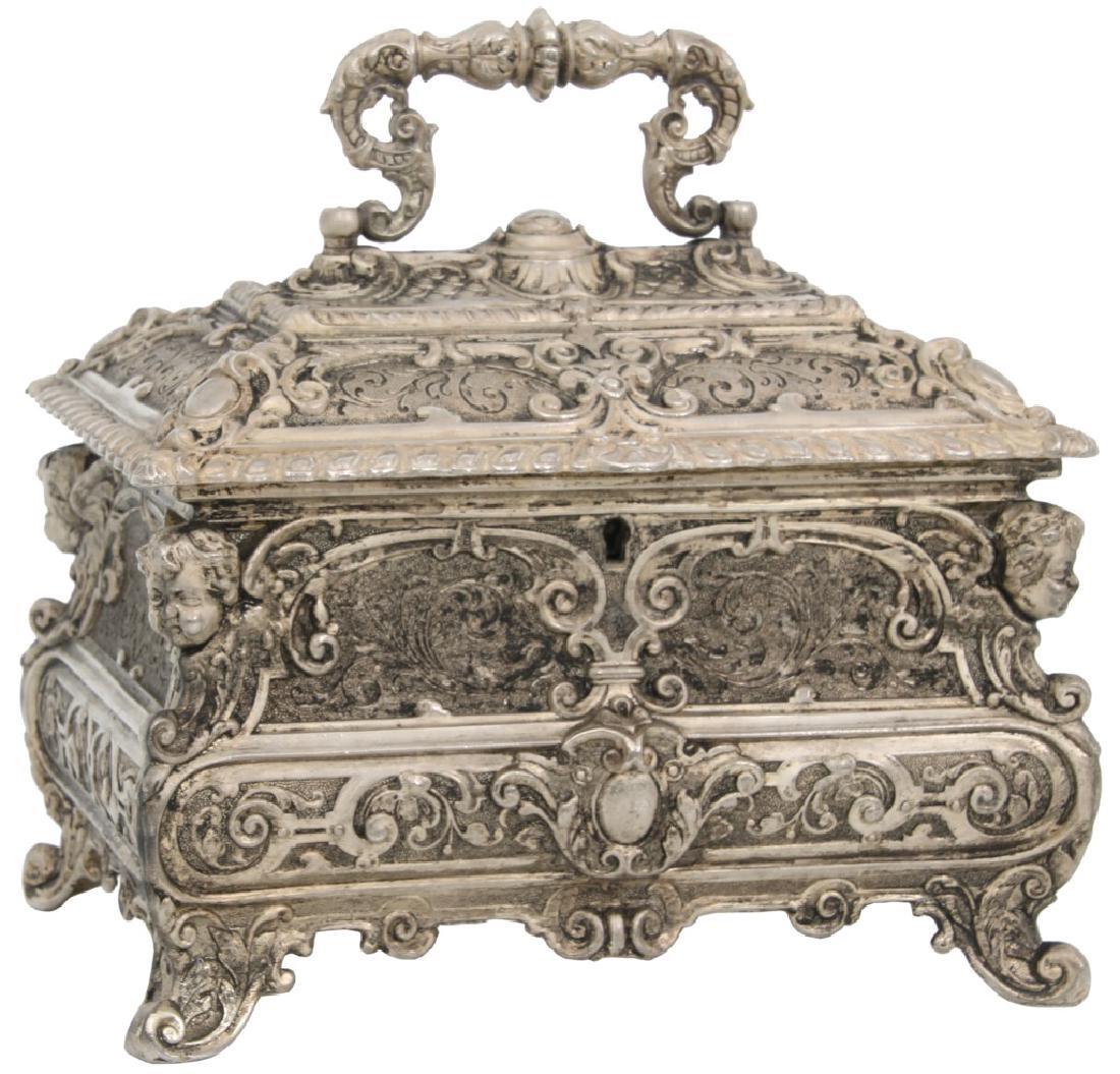 Silver Plated Jewelry Casket: Silver Plated Jewelry Casket. Hinged handle on top of the lid with allover relief filigree design and large winged putti heads at the corners; unsigned, interior is not lined. 7.75" high x 9" wide x 6