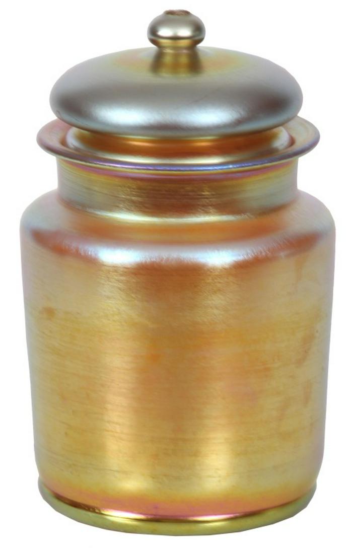 Tiffany Studios Covered Jar: Tiffany Studios Covered Jar. Gold iridescent Tiffany jar has a squared shoulder, flaring lip and cylindrical body; lid has a finial with a wheel-carved top surface. In good condition with no damage or