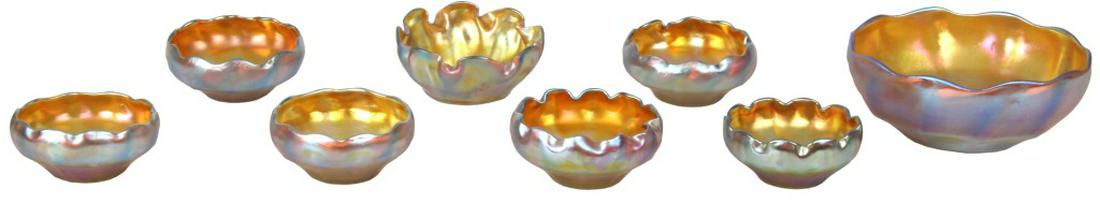 Eight Tiffany Studios Nut Bowls: Eight Tiffany Studios Nut Bowls. The larger gold iridescent art glass nut bowl has a wavy rim and is signed on the underside, “L. C. Tiffany - Favrile”; 3 in. high x 7 in. diameter. The seven smal