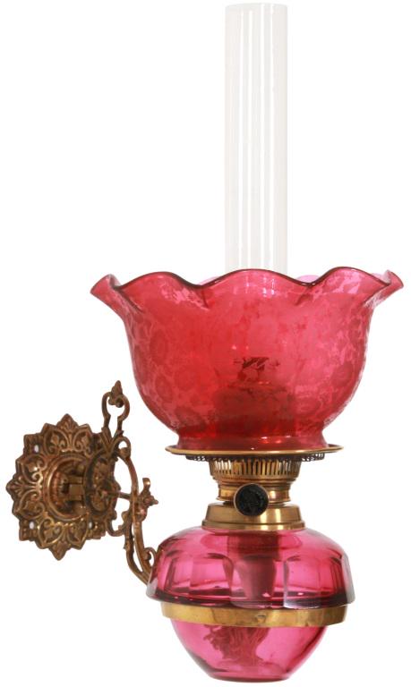 Brass & Cranberry Glass Oil Font Wall Sconce: Brass & Cranberry Glass Oil Font Wall Sconce. Relief decorated brass rosette-form wall plate with pierced filigree decorated brass arm and 4.25 in. diameter font ring; faceted cut cranberry glass oil 