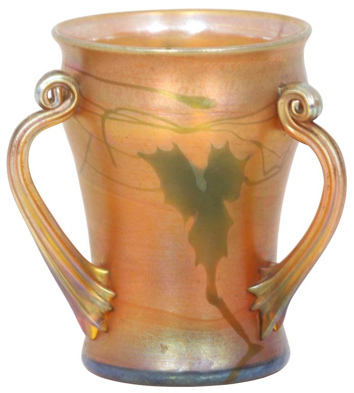 Tiffany Studios Favrile Glass Loving Cup: Tiffany Studios gold iridescent Favrile glass loving cup has three fluted and coiled handles, the body has a green pulled leaf and vine design; signed on the underside, L. C. Tiffany - Favrile, 9671C.