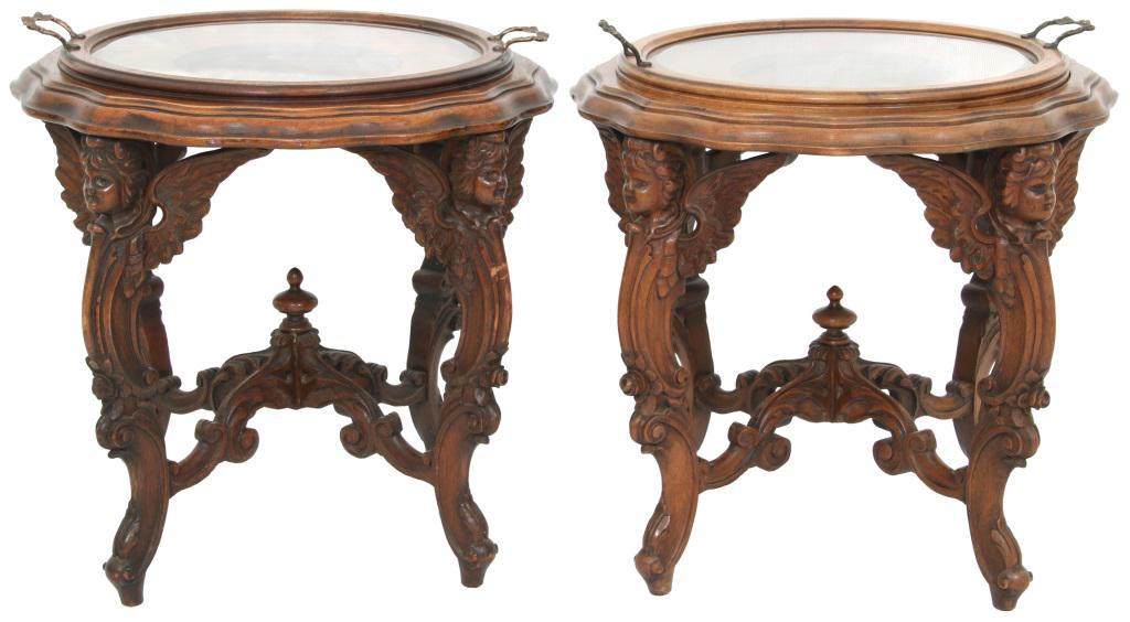 Two Figural Carved Walnut Serving Tables: The two serving tables have figures of cherubs on each leg with a center finial on the carved stretchers; removable serving tray on top over a central medallion of a female portrait with bronze figura