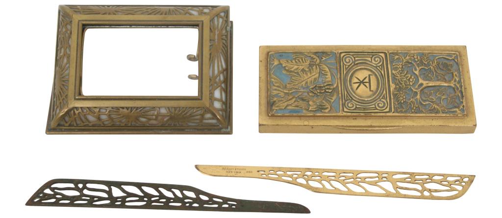 Four Tiffany Studios Desk Accessory Items: Tiffany Studios calendar holder is done in the pine needle pattern and has a glass front; signed on the underside, "Tiffany Studios, New York, 930." 1 in. high x 4.5 in. wide x 3.5 in. deep. Tiffany S