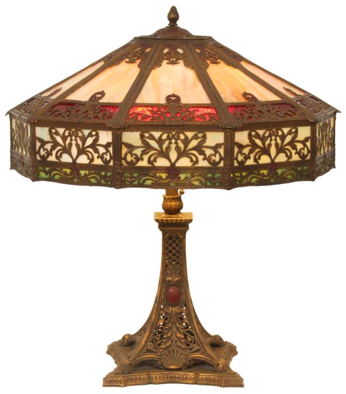 E. Miller Paneled Glass Lamp: E. Miller table lamp with an overlaid pierced decorated shade has four rows of different colored panels that include caramel, cranberry, blue and green. The base supporting the shade has shell motifs,