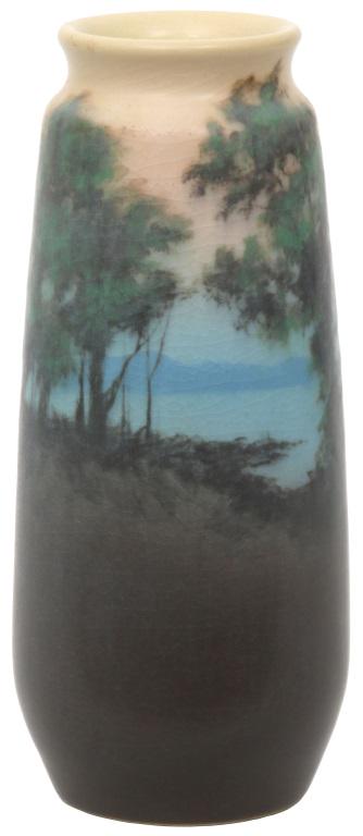 Rookwood Pottery Vellum Landscape Vase: Rookwood Pottery vase is decorated with a landscape scene having green trees in the foreground with blue water and mountains in the distance. Marked on the underside with flame mark dating it to 1915,