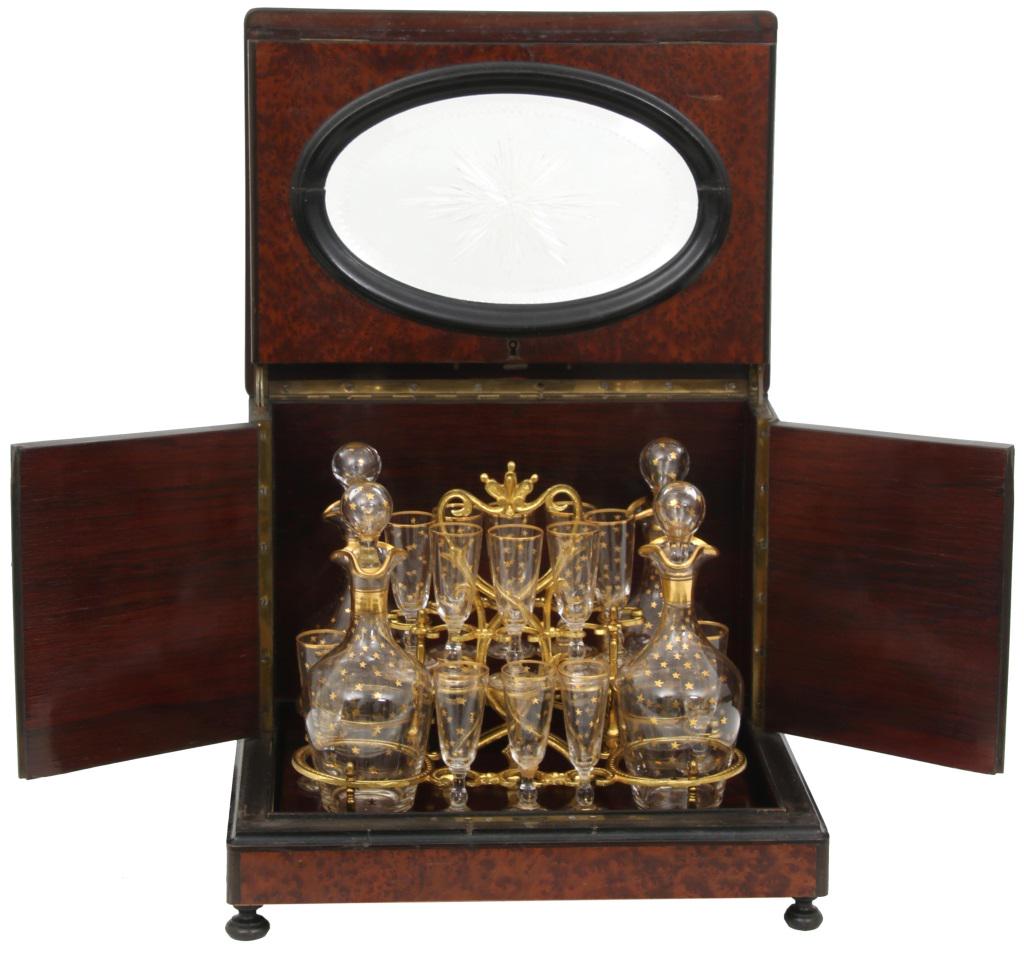 Birdseye Maple Tantalus: Birdseye maple tantalus with oval cut glass panels having sunburst motifs and zipper cut beveled glass, hinged top and sides opening to a gold painted decanter and glass set with star decoration. 11 i