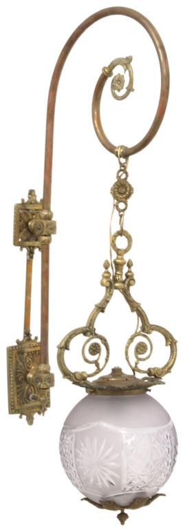 Brass & Cut Glass Wall Sconce: Wall sconce with a brass fixture having a curling arm, filigree decoration and pineapple finials, supporting a cut glass globe, 34 in. high x 9 1/2 in. wide x 13 in. deep.