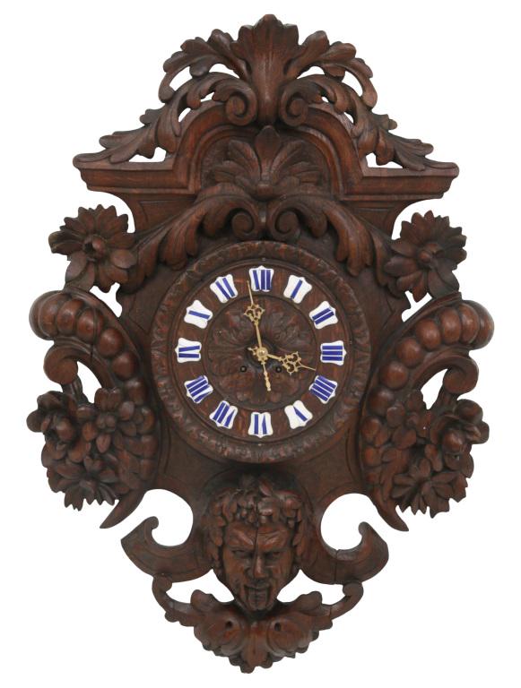 Figural Carved Oak Wall Clock: Wall clock with a heavily caved oak case having flowers and a mythical creature head, dial with applied porcelain panels and blue Roman hour numerals, 8-day brass movement with count wheel striking on
