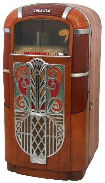 Rock-Ola Model 1426 Jukebox: Rock-Ola Model 1426 Jukebox, circa 1947, with wood grained veneer case having ribbed amber plastics on the corners and across the crest, colorful rotating cylinders behind the side panels, grill with 