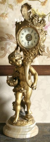 Jennings Bros Figural Desk Clock: Black spade hands and Arabic numerals in a porcelain dial. The movement is contained in a cornucopia that the putti holds in his left hand and a basket of fruit in his right; on a small onyx base. 18"