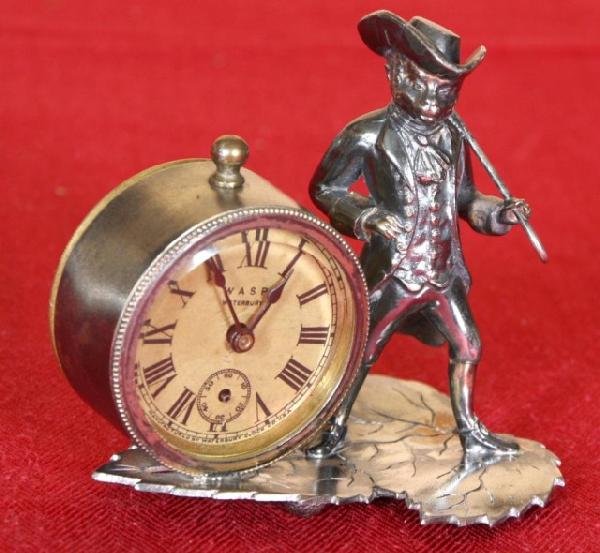 Waterbury Silver Plated Figural Novelty Clock: Waterbury Silver Plated Figural Novelty Clock. The Figure of a monkey wearing a suit and a top hat with a cane stands next to the time piece. Has a paper dial, blue spade hands; all on a leaf shaped p