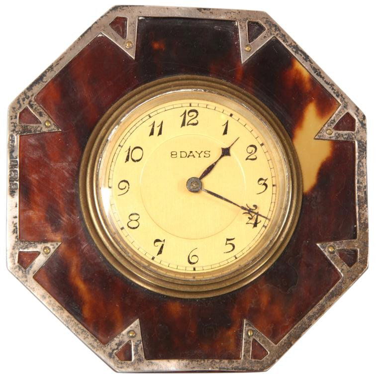 English Sterling & Tortoise Clock: English Sterling & Tortoise Clock. Octagonal desk clock has a tortoise shell front with sterling frame and overlay on the front; yellow dial has Arabic numbers and fancy hands, 8 day spring driven mov