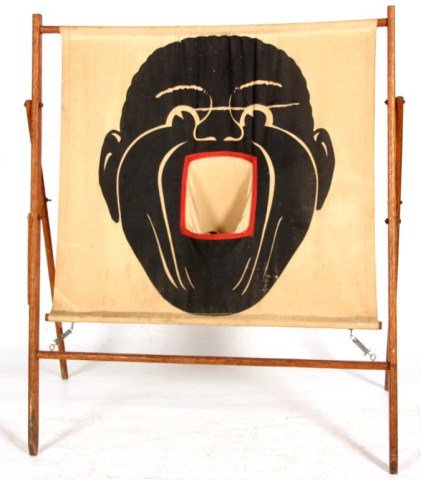 Black Face Canvas Carnival Game: Black Face Canvas Carnival Game. The standing spindled wooden tripod stretches a large canvas painted with a black face, the open mouth contains a pocket to catch balls. Signed 10-x Baseball Target, P