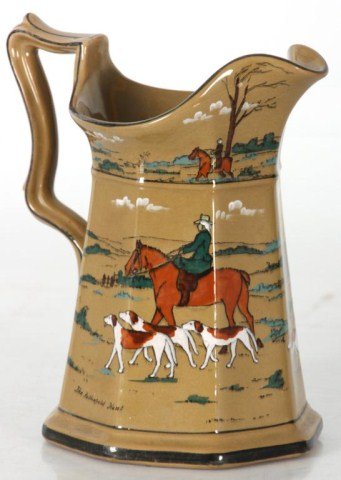 Deldare Ware Pottery Pitcher: Deldare Ware Pottery Water Pitcher. Has a hexagon shape with fancy handle and wavy rim; painted with hunting scenes. Buffalo Pottery mark on base; single hairline in the rim. 8 in. high