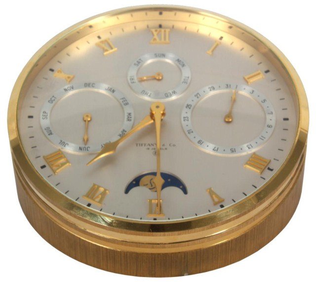 Tiffany & Co Desk Clock: Tiffany & Co Desk Clock. Gilt brass desk clock, has a 5 in. silvered dial with applied gilt brass Roman hour numerals and hands. 4 sub dials for Day, Date, Month and Moon Phase. 15 Jewel, 8 day moveme