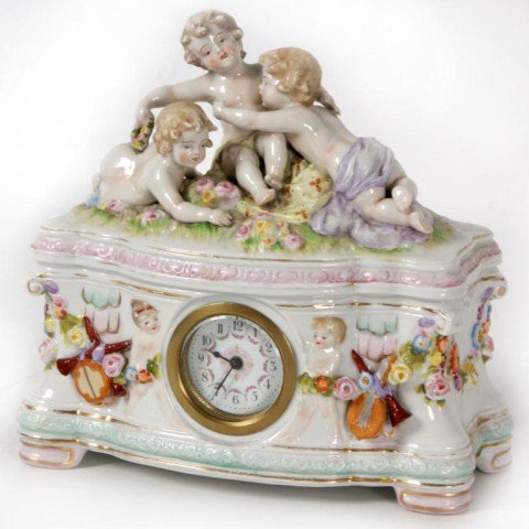 Figural Porcelain Desk Clock: Figural Porcelain Desk Clock. 3 Figural putti are playfully arranged on the top, 1.5 in. enameled dial centered on the front of the case. Blue mark on the back. 8.25 in. High x 8.5 x 4. in good condit