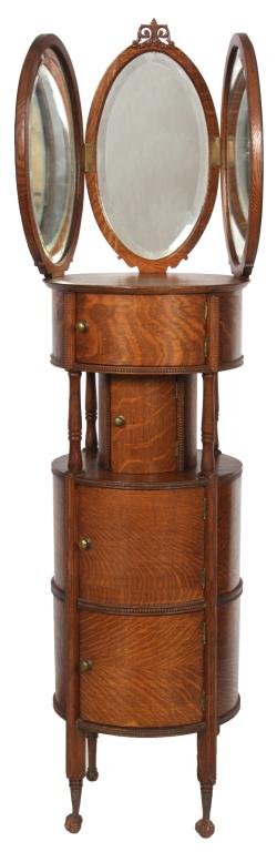 American Oak Shaving Stand: American Oak Shaving Stand. Oval and beveled, triple mirrored top with pierced carved crest; has a cylindrical body with 4 doors, turned columns around the inset center section and stands on turned fe