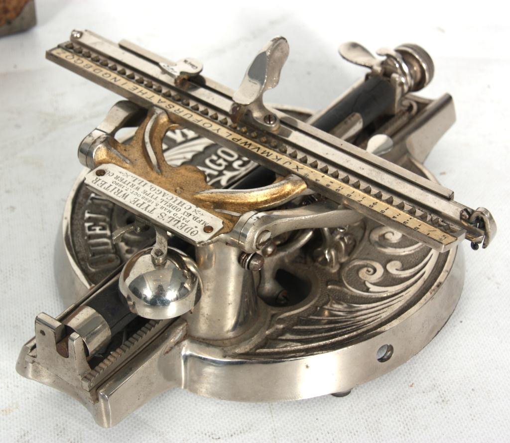 Odell's Typewriter No. 2 In Case: Odell's Typewriter No. 2 in Case. Cast base has a silvered finish with swirling filigree design in the unusual round base and signed Odell Type Writer, Chicago, Illinois. The number 2 was the first mo