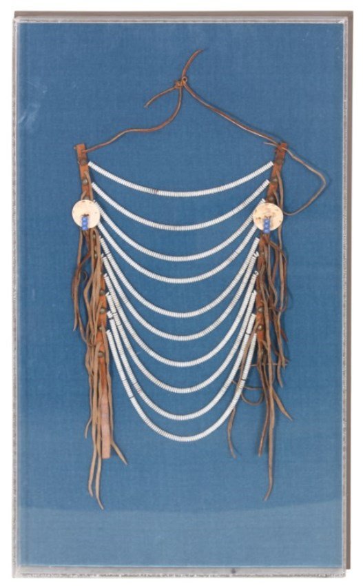 Native American Beaded Necklace: Native American Beaded Necklace. 10 Graduated strands of white beads fixed with brass rivets along vertical leather straps with hanging tassels. Framed and protected in a plexiglass case. 29 in. high