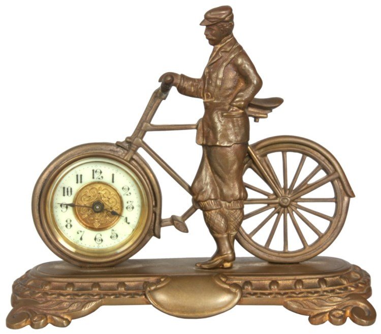 British United Clock Co. Bicycle Clock: British United Clock Co. Bicycle Clock, c.1900-1910. Cast brass case has the figure of a man standing beside a bicycle facing left. The front wheel contains the timepiece with dial having a 1.75 in. p