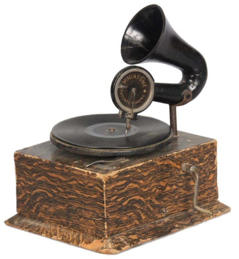 Miniaphone Toy Phonograph: Miniaphone Toy Phonograph. Has a wood box with faux wood printed paper covering, 5.5 in. turntable with horn and Miniaphone reproducer. Spring winds and turntable works, has on-off switch, some wear t