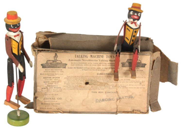 Dancing Rastus Talking Machine Toy: Dancing Rastus Talking Machine Toy. Standing wooden figure of ragtime rastus designed to mount on a talking machine (phonograph), the figure stands on a platform, dances and kicks his legs as the turn