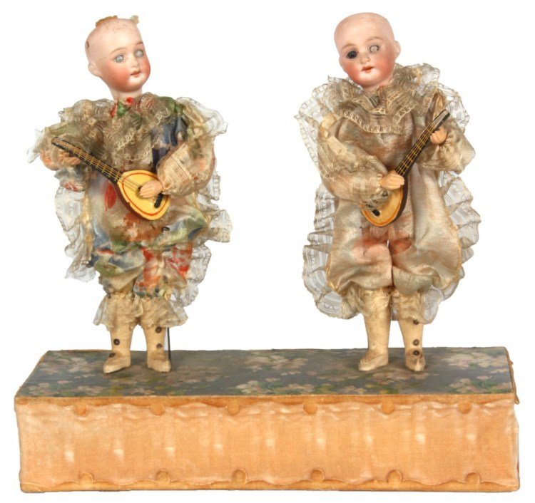 Hand Operated Doll Automaton: Hand Operated Doll Automaton. Double standing doll figures with lace and silk clothing both playing a stringed instrument, figures have bisque heads marked "Made in Germany 12/0" with carved wood bodi