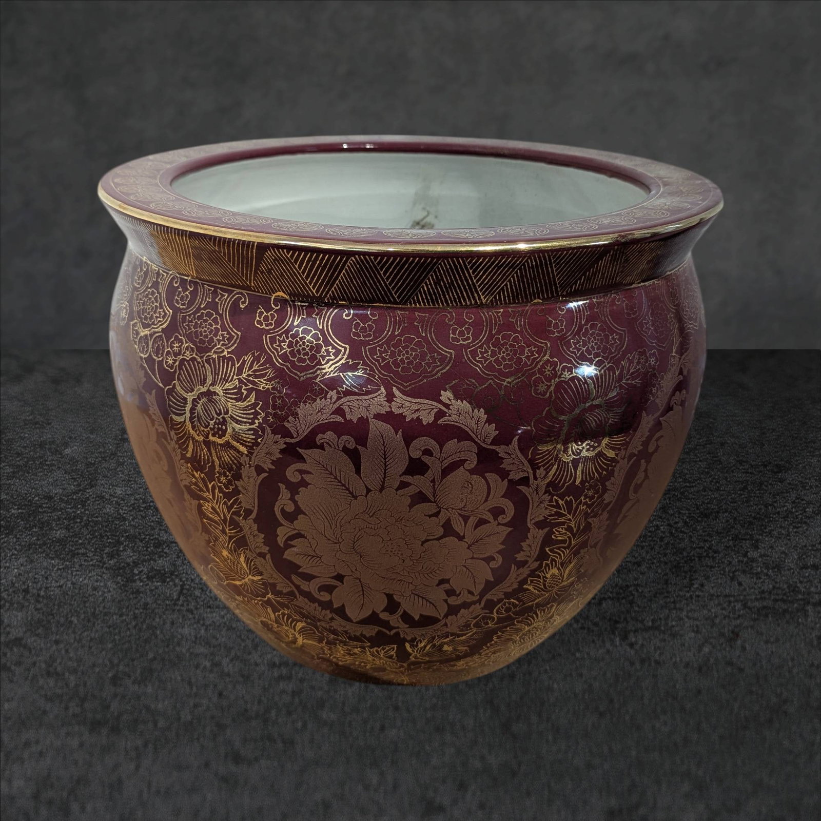 Chinese Porcelain Jardiniere with Gilded Decoration and Painted Interior: A 12-inch-tall Chinese porcelain jardiniere with a 14 1/4-inch diameter. The exterior features a burgundy glaze adorned with intricate gilded floral and geometric patterns, while the rim is decorated 