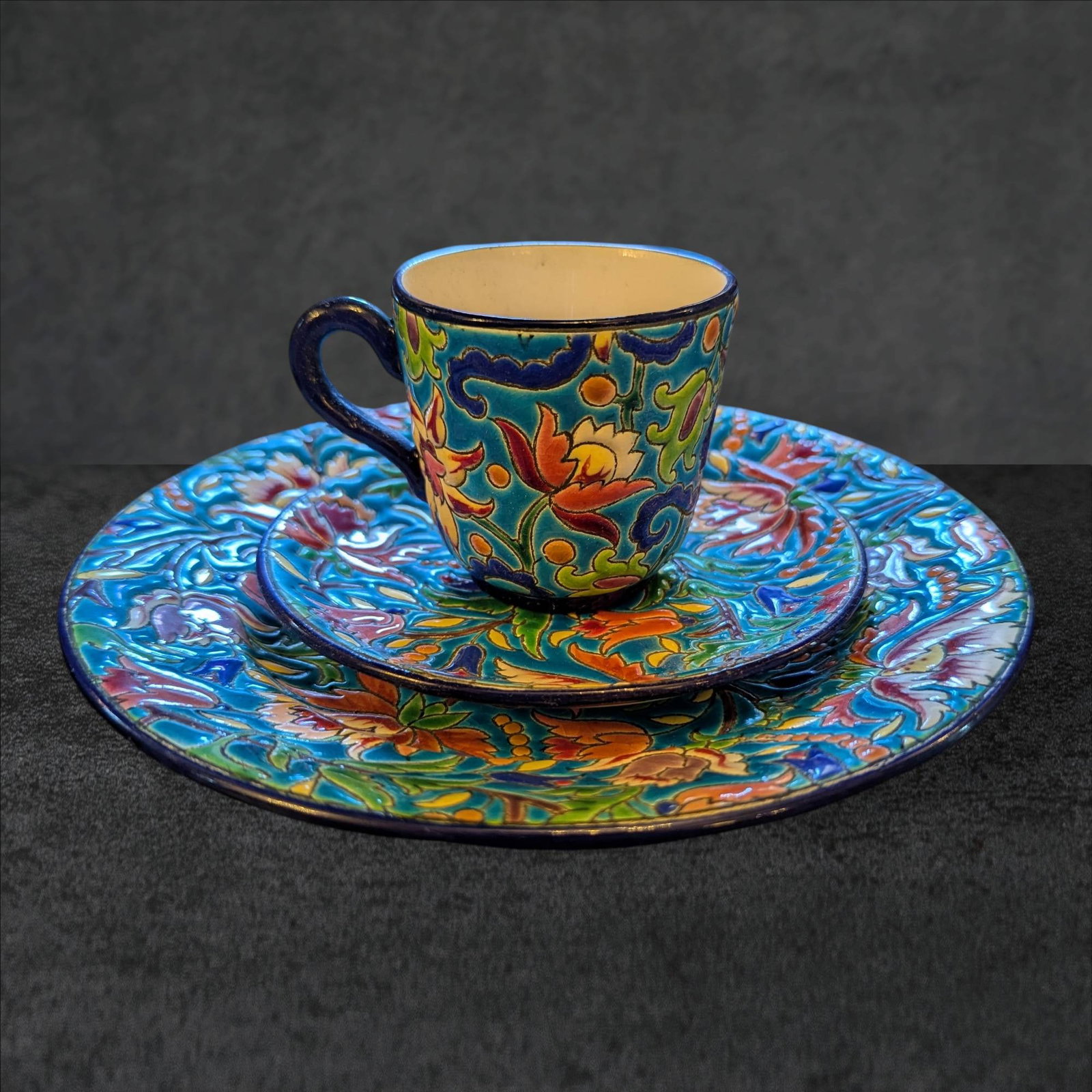 Two Emaux de Longwy Hand-Painted Enamel Porcelain Luncheon Settings: Two sets of luncheon settings, each comprising a teacup (3 in tall, 3 in diameter), saucer (5 in diameter), and plate (8 in diameter). Each piece features vibrant, hand-painted floral motifs in enamel