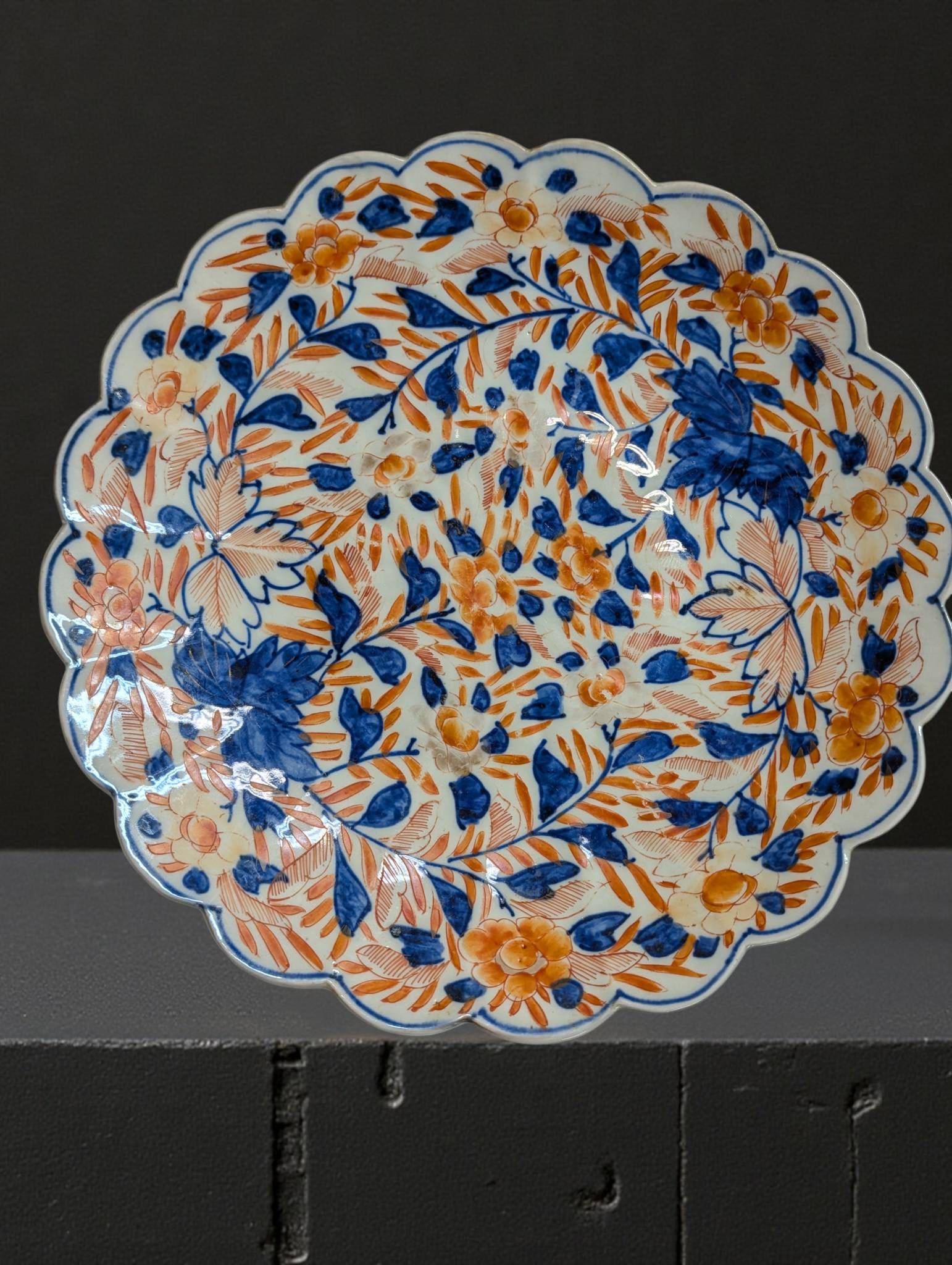 19th Century Imari-Scalloped Porcelain Plate with Hand-Painted Floral Design: Imari- porcelain plate from the 19th century, featuring a scalloped edge and hand-painted floral and leaf designs in cobalt blue and iron red (orange) with gold gilding on a white ground. The style ec