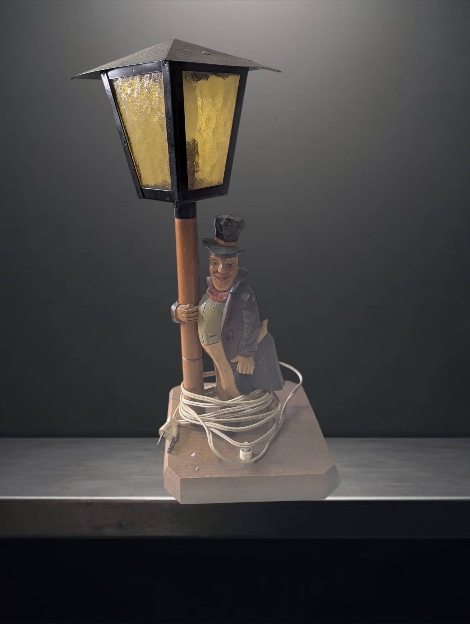 Black Forest Wood-Carved Music Box with Drunken Man and Lamppost: Black Forest wood-carved music box depicting a drunken man leaning on a lamppost. The lamp features a functional light with a yellow stained-glass-style shade. The base, measuring 7 in by 7 in, houses