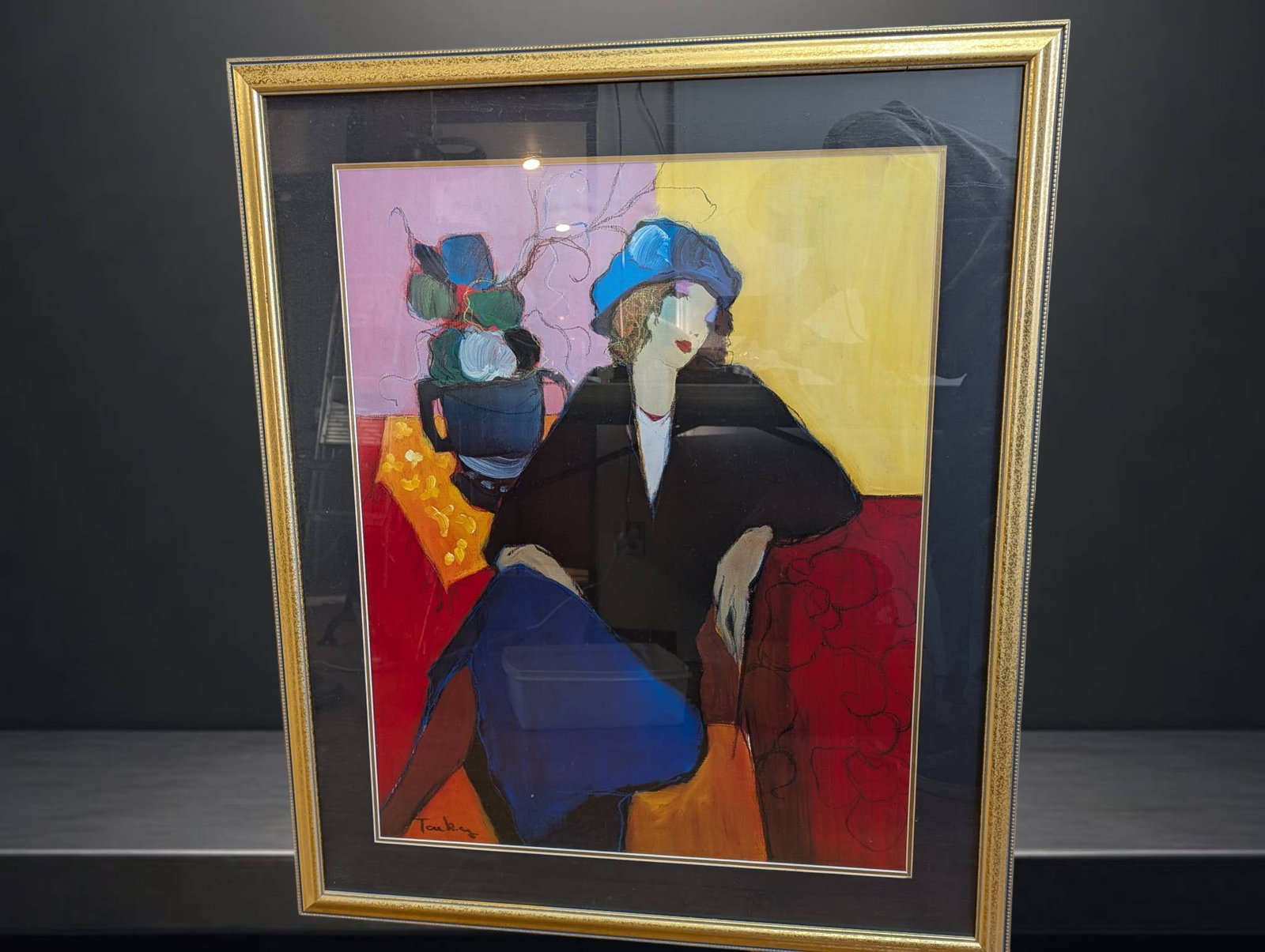 Framed 39 in by 32 in Print of Stylized Seated Woman: Colorful 39 in by 32 in print depicting a stylized seated woman against a vibrant yellow and red background. The figure is adorned with a blue hat and is surrounded by abstract elements, including a v