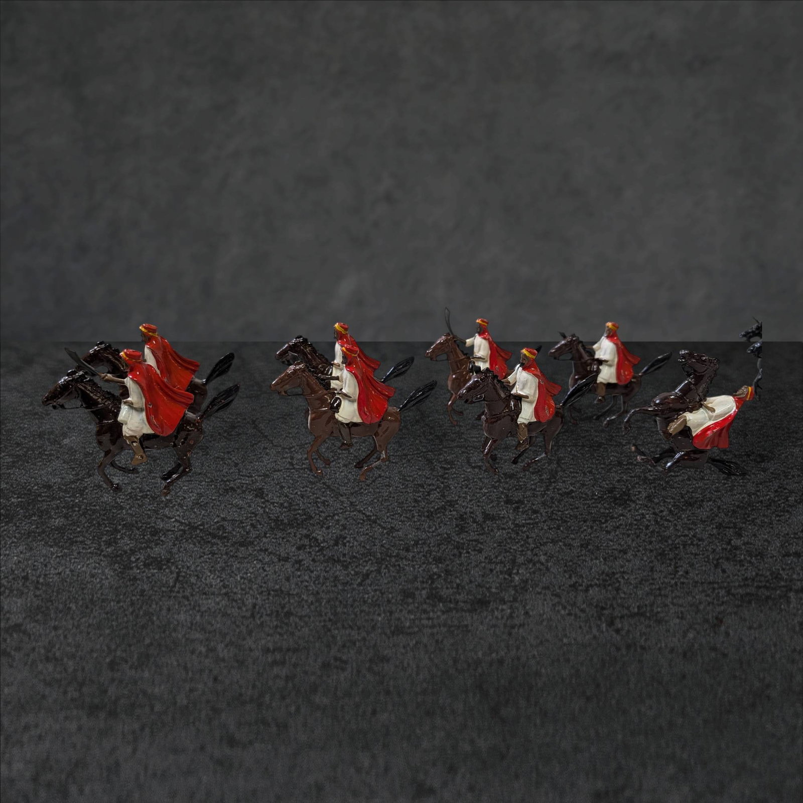 8 Britain LTD Arab Figures on Horseback: Eight painted metal figures by Britain LTD depicting Arab riders on horseback. Each figure features detailed craftsmanship with red cloaks and white garments. The set includes eight individual riders,