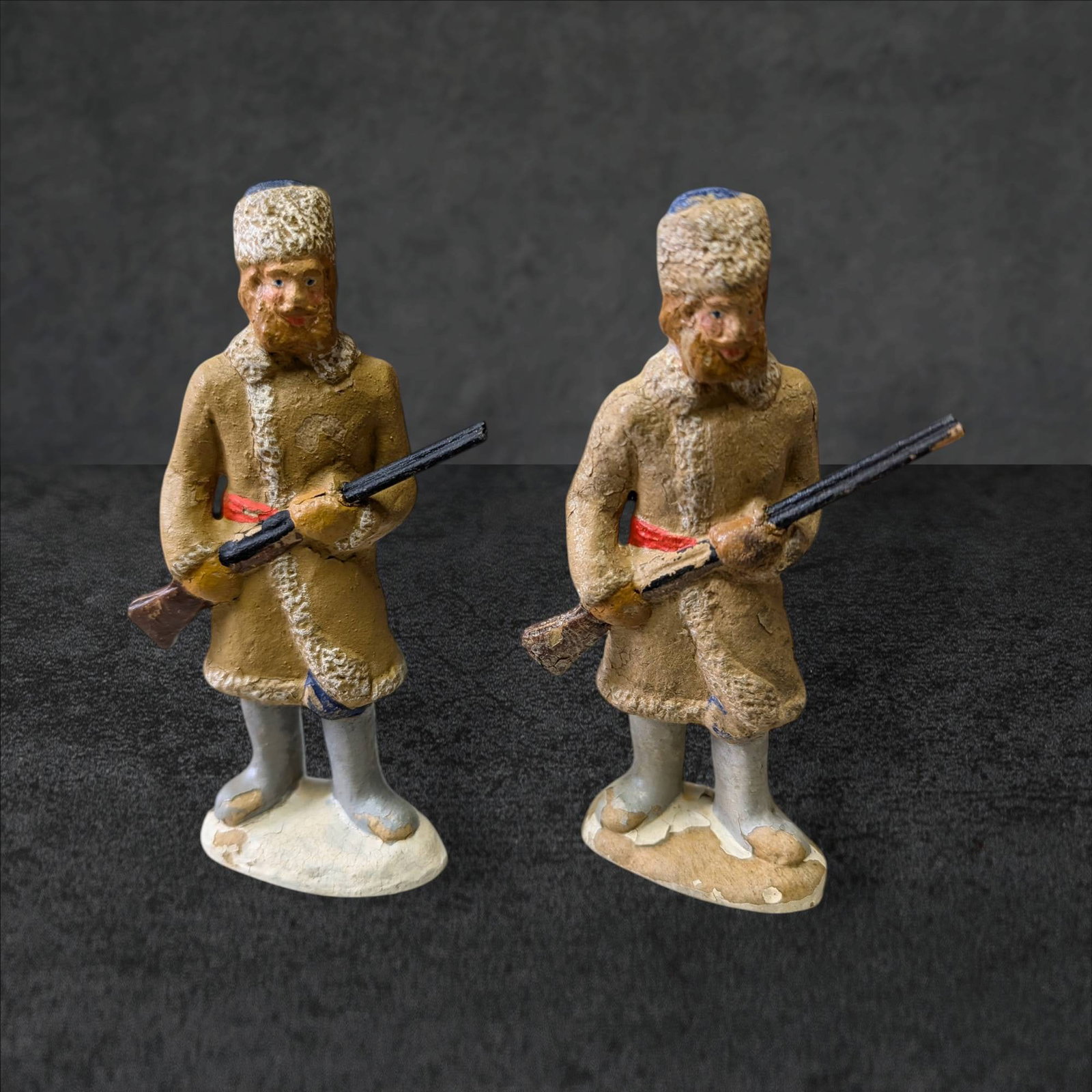 Hand-Painted Sawdust and Glue Mountain Men Figurines, 4.5 Inches Tall: Two hand-painted figurines of mountain men, constructed from sawdust and glue. Each figure measures 4.5 inches tall and is depicted holding a rifle. The men wear fur-trimmed coats, hats, and feature d