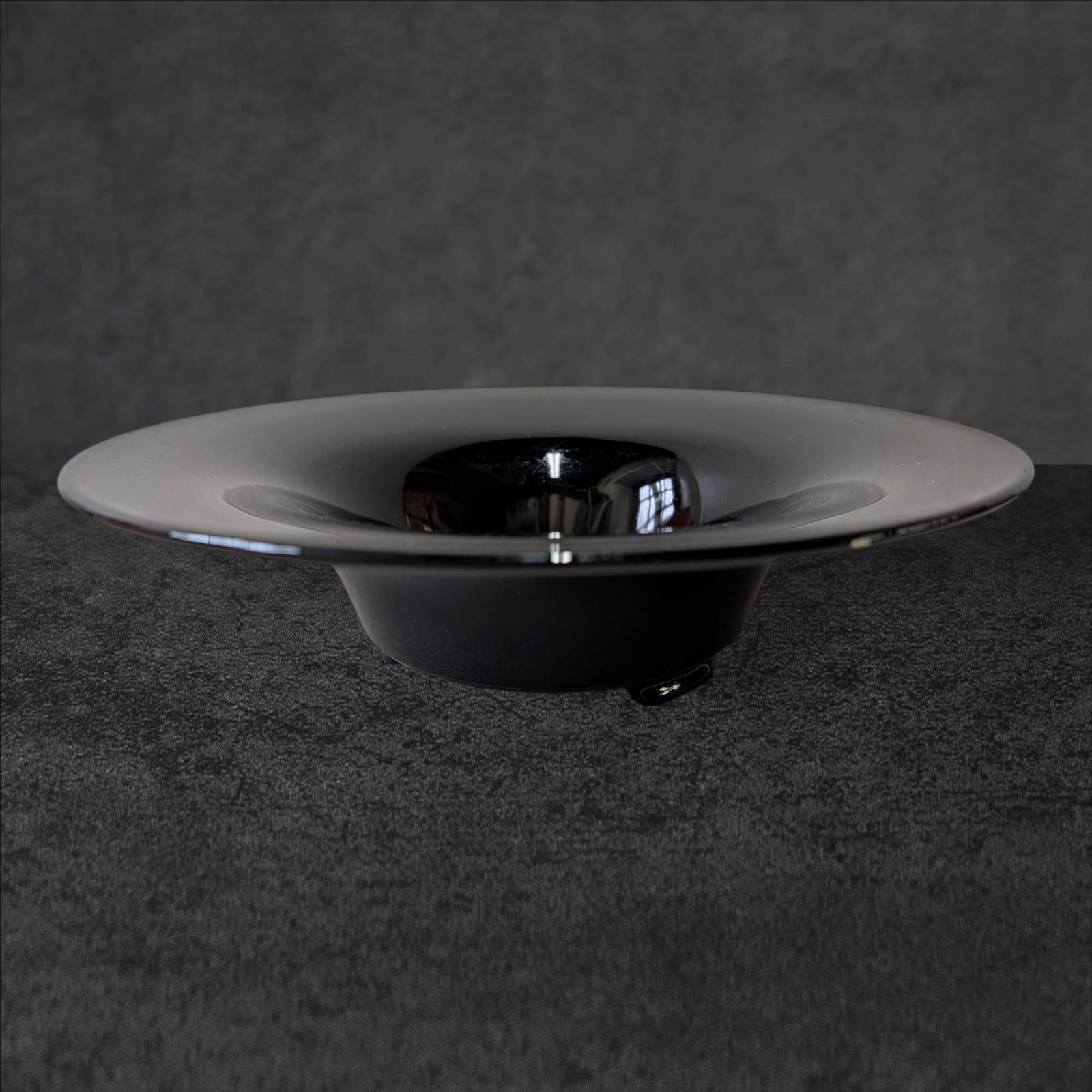 Footed Black Amethyst Glass Bowl, 12 Inches in Diameter: Footed black amethyst glass bowl measuring 12 inches in diameter and 3 1/4 inches tall. Features a wide, shallow design with a flared rim and a central elevated base with three support points. The gla
