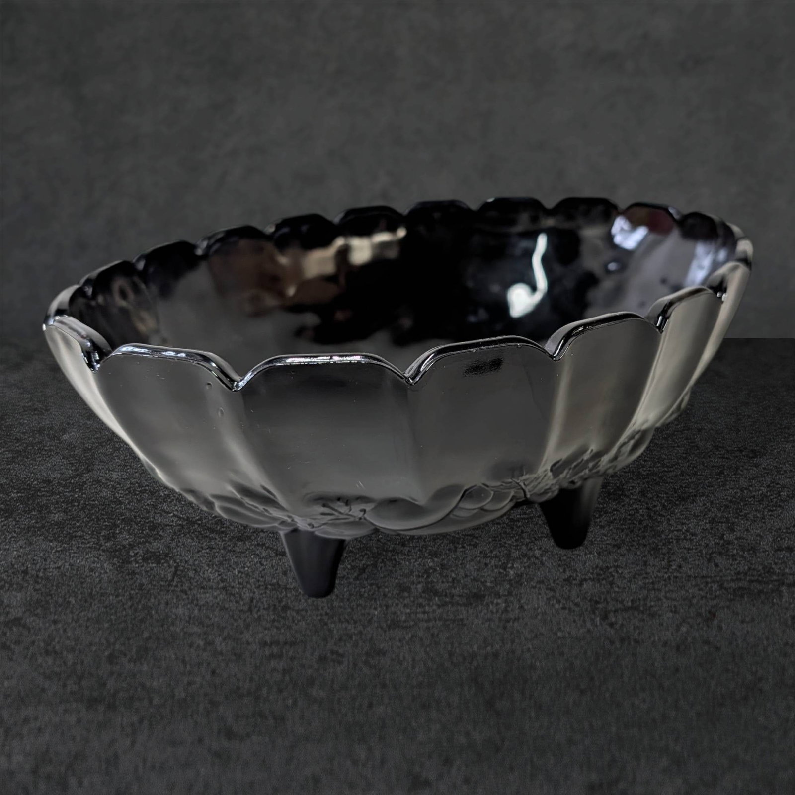 Footed Black Amethyst Glass Bowl, 12 1/4 In. x 8 1/2 In. x 4 1/2 In.: Footed black amethyst glass bowl featuring a scalloped rim and fruit-themed decorative elements. Measures approximately 12 1/4 inches in length, 8 1/2 inches in width, and 4 1/2 inches in height. The 