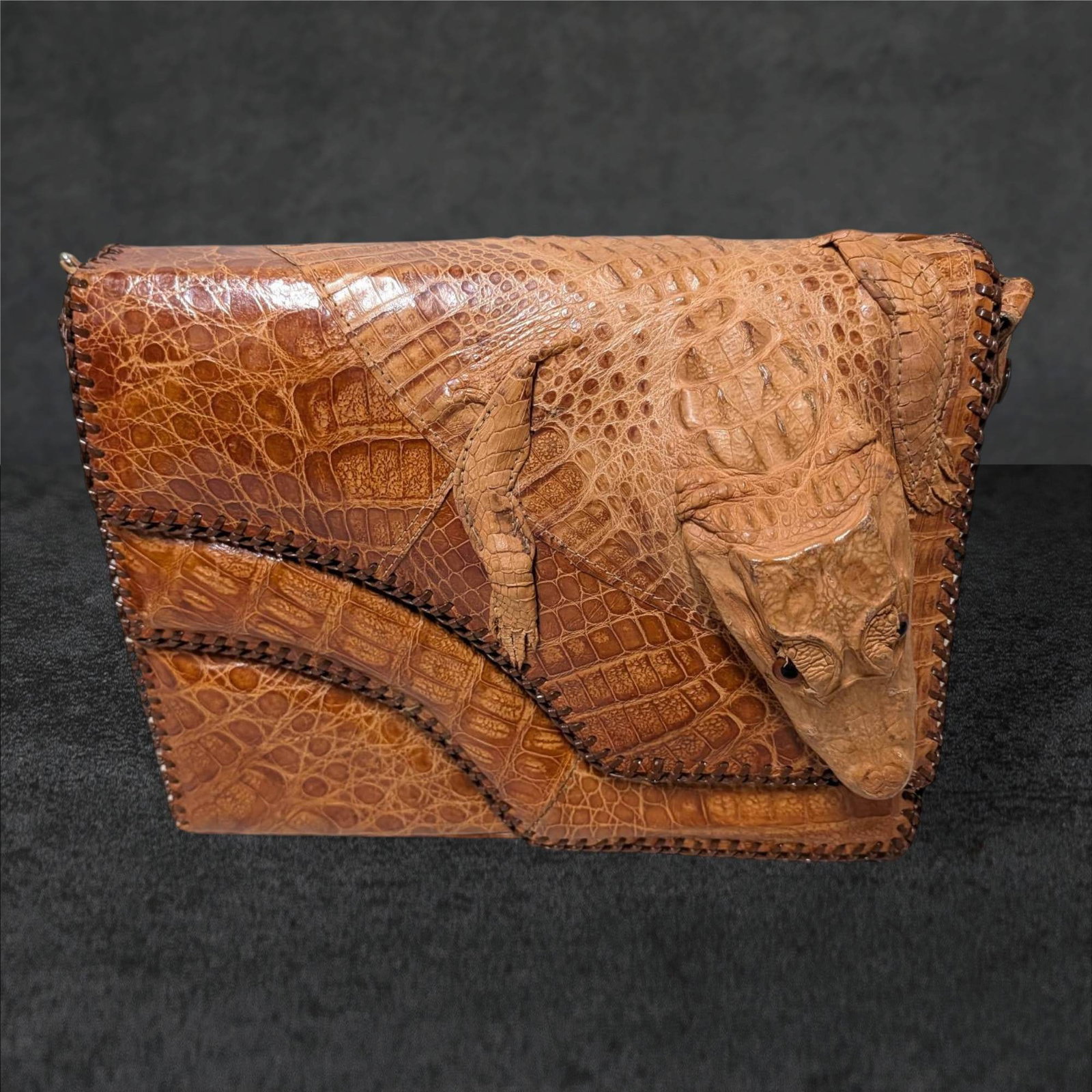 1950s Alligator Purse with Sculpted Design, Made in the USA: A handmade 1950s alligator purse featuring a sculpted alligator detail on the flap. Crafted in the USA, it measures 12 in by 8.5 in by 3 in. The interior has multiple compartments and is lined with a 