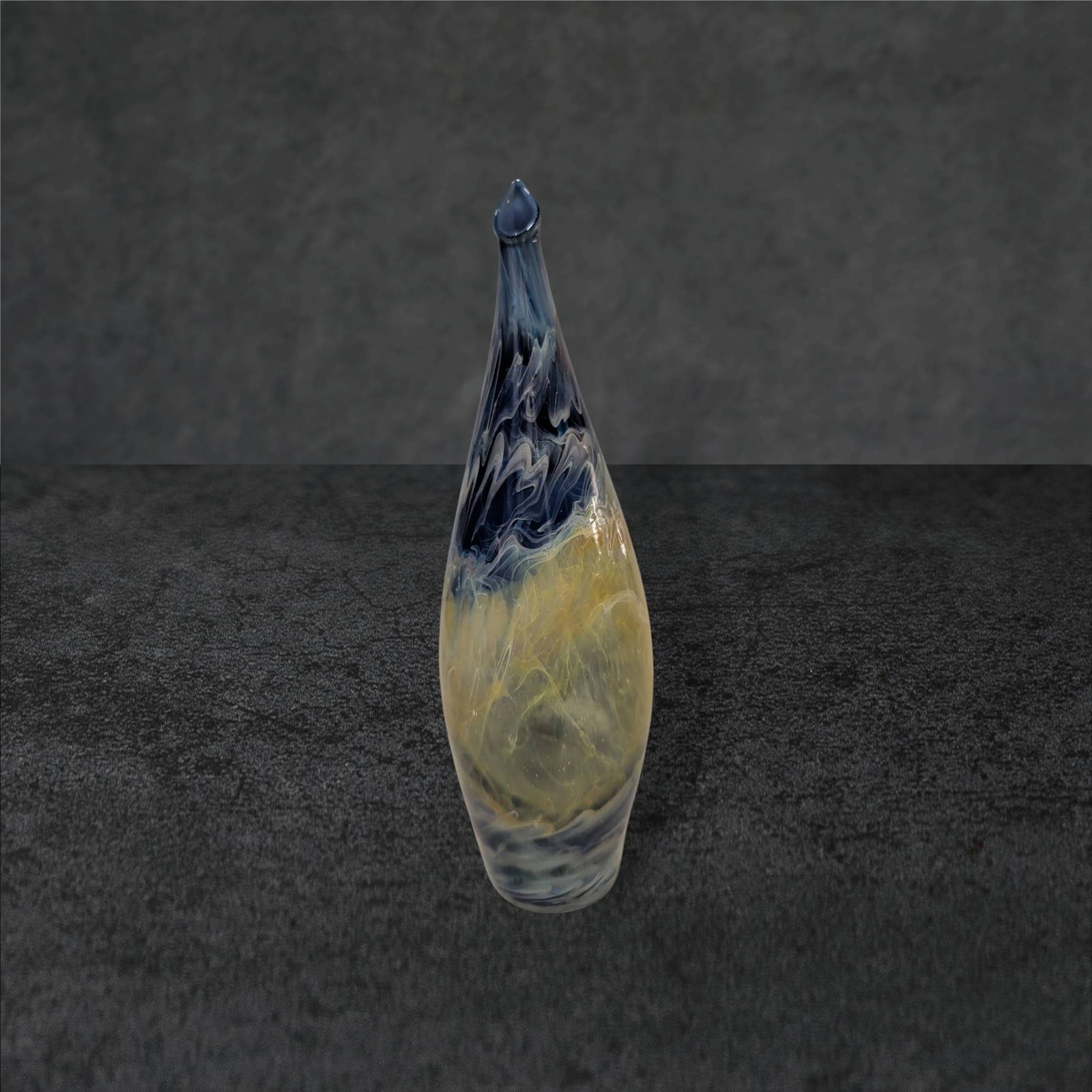 Tall Hand-Blown Glass Vase with Swirled Blue and Yellow Pattern: Hand-blown glass vase featuring a smooth, elongated form with a pointed tip. The design showcases swirled patterns in shades of blue and yellow, creating a dynamic, flowing effect. The vase has a glos