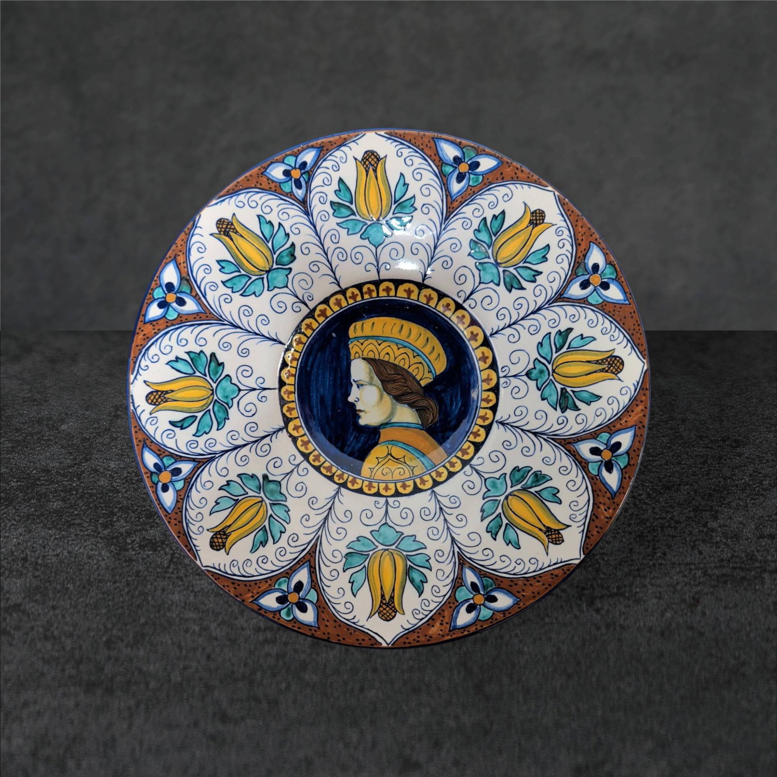 Hand-Painted Ceramic Plate Featuring Renaissance Style Portrait, 9.5 in: Hand-painted ceramic decorative plate with a Renaissance-style female portrait at the center, surrounded by floral and botanical motifs in yellow, blue, and green over a white background. The reverse 