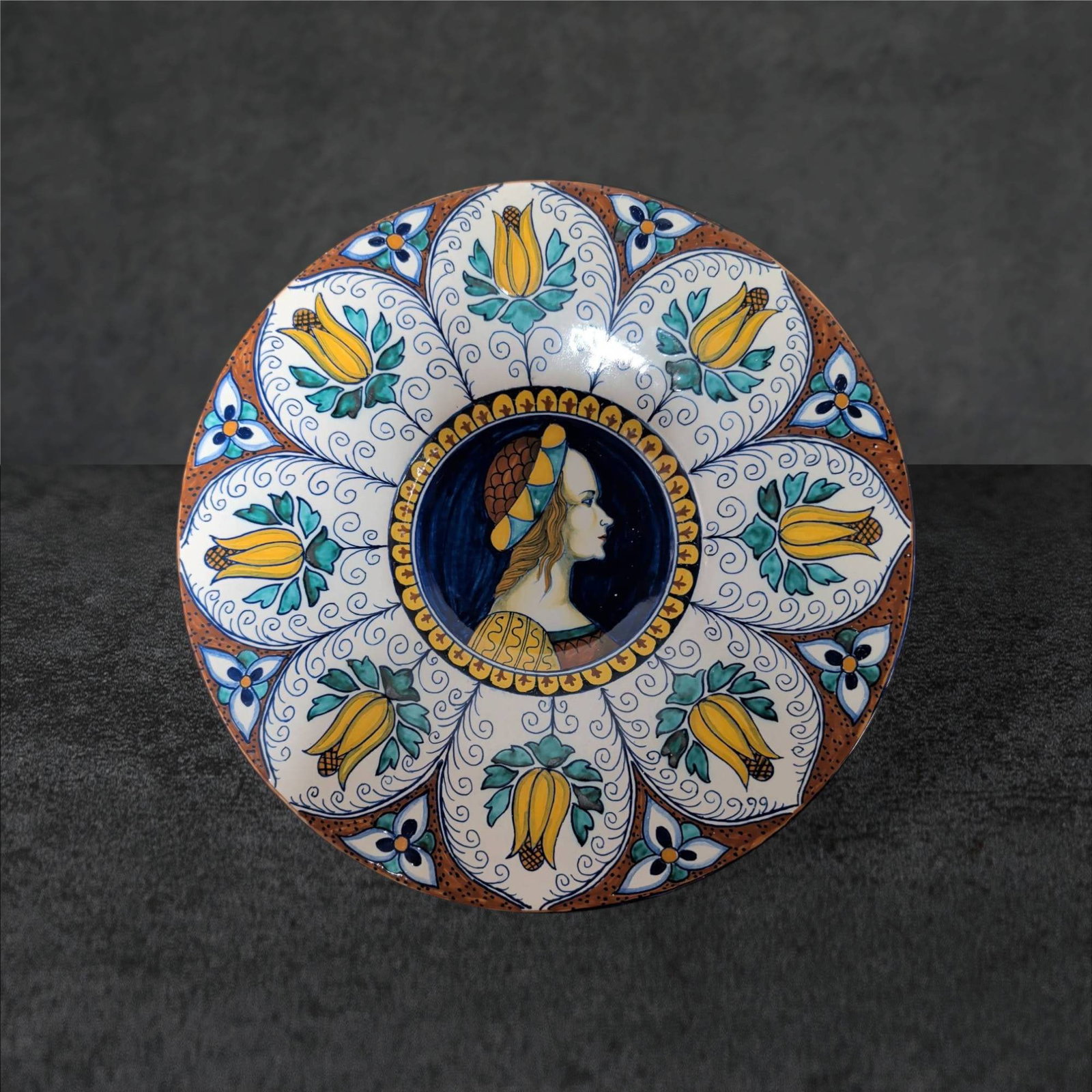 Hand-Painted Ceramic Plate with Portrait and Floral Motif, 9.5 Inches in Diameter: Decorative ceramic plate featuring a hand-painted central portrait of a woman framed by a segmented floral design in vibrant colors, including yellow, green, and blue. Measures 9.5 inches in diameter.